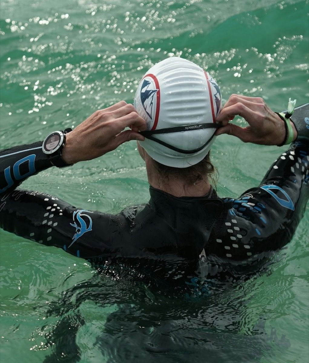 Open-water swimmer in a wetsuit adjusting goggles before a swim